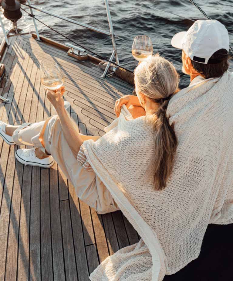 An image of a retired couple enjoying wine on the deck of a boat at sunset.